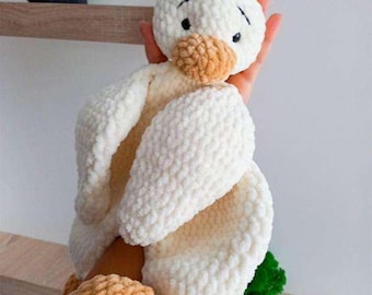 May include: A handmade, plush white duck toy with a light brown beak and feet. The duck has black eyes and a fluffy, textured appearance. The toy is held in a person's hands, showcasing its soft, cuddly design. A charming, handcrafted item.