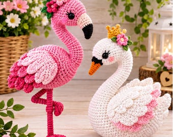 May include: A pink crochet flamingo standing on one leg with a floral headpiece and a white crochet swan wearing a yellow crown and a floral headpiece. Both figures feature detailed stitching, black eyes, and layered wing textures in yarn.
