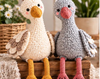 May include: Two handmade crochet stuffed birds sitting side by side. The left bird is cream-colored with brown wing accents and yellow webbed feet. The right bird is gray with a pink beak and pink webbed feet. Both have black eyes and pink cheeks.