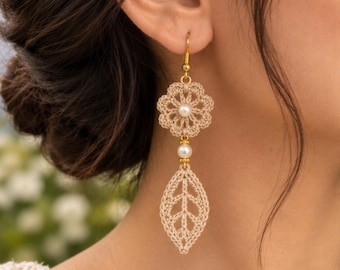 May include: A beige crochet earring featuring a flower-shaped top with a central white pearl, a small gold-toned bead, and a dangling leaf-shaped crochet element. The earring is attached to a gold-toned hook and showcases intricate thread work.