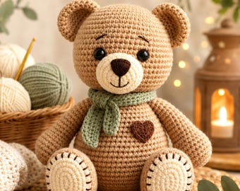 May include: A tan crochet teddy bear featuring a light cream muzzle, a dark brown nose, and a small brown heart patch on its chest. The bear wears a sage green crocheted scarf and has light cream circular patches on the soles of its feet.