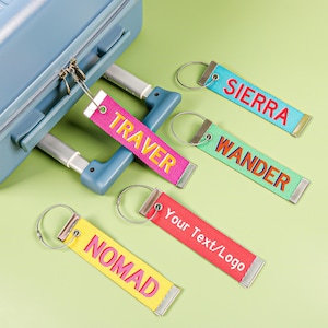 Peut inclure: Plusieurs étiquettes de bagages colorées avec des mots tels que "SIERRA", "WANDER", "NOMAD" et "TRAVER". Chaque étiquette rectangulaire est dotée d'un anneau métallique et d'une sangle en tissu. Une étiquette indique "Your Text/Logo".