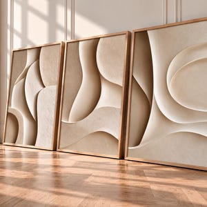 May include: A set of three rectangular wall art pieces framed in light wood, each featuring a beige and cream abstract design with smooth, flowing, layered curves that create a sense of depth and dimension across the three separate panels.