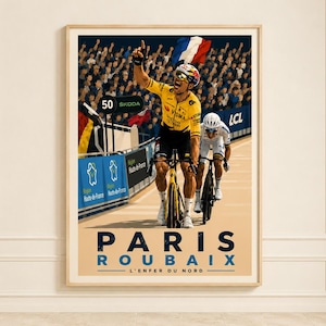 Op de afbeelding: Een ingelijste poster met een wielrenner in een geel shirt die één arm in de lucht steekt als overwinning op een baan. De tekst PARIS ROUBAIX L'ENFER DU NORD staat onderaan. Een menigte is zichtbaar op de achtergrond met een Franse vlag.