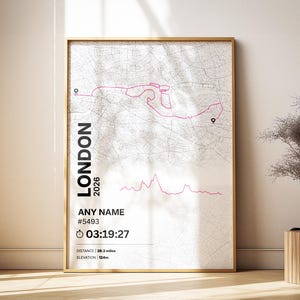 May include: Framed map art print featuring a pink route over a detailed gray map of London. The print includes the text "LONDON 2026" and customizable fields for a name, race number, and time. The distance is 26.2 miles, and the elevation is 124m.
