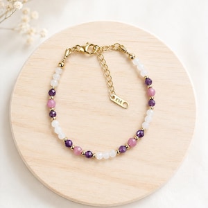 May include: A delicate bracelet featuring alternating white, purple, and pink faceted beads interspersed with small gold-toned metal spheres. The piece includes a gold-toned chain extender with a small tag clearly engraved with the text K14.