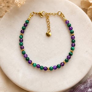 Peut inclure: Un bracelet de perles composé d'une alternance de perles rondes en malachite verte et en améthyste violette, agrémenté de petites perles intercalaires en métal doré. Le bracelet comprend un fermoir mousqueton doré, une chaînette et un petit cœur.