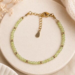 Peut inclure: Un bracelet délicat composé de petites perles facettées vert clair alternées avec des perles métalliques dorées lisses et rondes. Le bijou comprend une chaînette d'extension dorée, un fermoir mousqueton et une petite breloque métallique en forme de goutte.