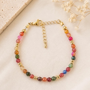 Op de afbeelding: Een armband met kleine, gefacetteerde, veelkleurige edelsteenkralen afgewisseld met gepolijste goudkleurige metalen tussenkralen. De armband is voorzien van een goudkleurige karabijnsluiting en een verstelbare verlengketting met een klein metalen hangertje.