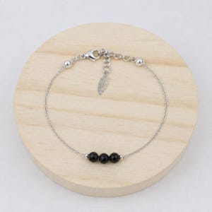 Puede incluir: Una delicada pulsera de cadena plateada con tres pequeñas cuentas negras facetadas centradas. La pulsera incluye un cierre de mosquetón, una cadena extensora corta y un pequeño dije plateado en forma de hoja que cuelga del extremo.