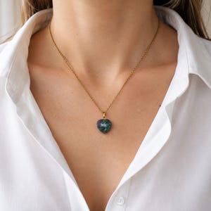 Peut inclure: Un collier à chaîne dorée avec un petit pendentif en forme de cœur. Le pendentif est composé d'une pierre polie à l'aspect marbré, présentant des nuances profondes de vert forêt, de bleu sarcelle et de rose magenta vif sur toute la surface.