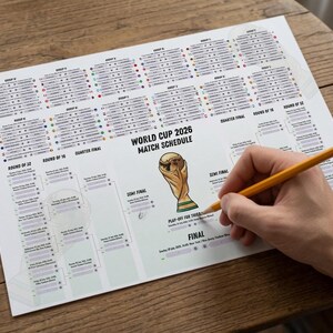 May include: A white paper World Cup 2026 match schedule featuring a central illustration of the gold trophy, group stage tables, and a tournament bracket. A yellow pencil is positioned on the sheet, which includes text for the final match.