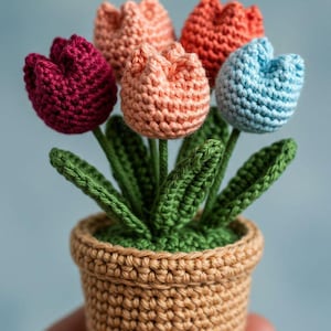 May include: A handmade crochet flower pot with five colorful tulips. The tulips are in shades of red, orange, and blue. The pot is a light brown color, and the leaves are green. The entire piece is held in a hand.