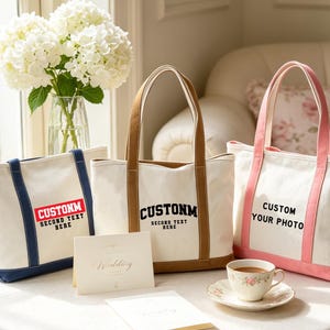 Peut inclure: Trois sacs fourre-tout en toile avec des anses et des bases colorées. Le sac de gauche a des accents bleus et le texte CUSTOMM SECOND TEXT HERE. Le sac du milieu a des accents marron et le texte CUSTOMM SECOND TEXT HERE. Le sac de droite a des accents roses et le texte CUSTOM YOUR PHOTO.
