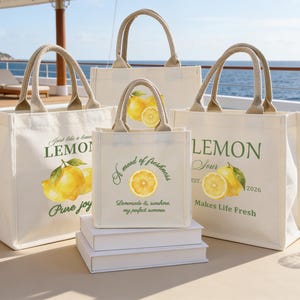 May include: Four off-white canvas tote bags with beige handles, each featuring a lemon-themed design. The bags have text and watercolor illustrations of lemons. One bag reads "Pure Joy", another "A mood of freshness", and a third "Makes Life Fresh".