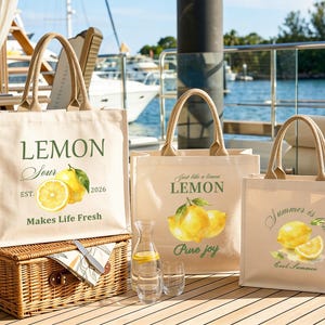 May include: Three canvas tote bags with lemon graphics and text. The bags have beige fabric, brown handles, and various lemon-themed phrases. One bag reads "Lemon Sour Makes Life Fresh". Another says "Just like a lemon Pure joy". The third says "Summer is here Cool Summer".