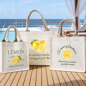 May include: Three canvas tote bags with beige handles and lemon graphics. One bag reads "Lemon Sour" with a lemon illustration and "Makes Life Fresh." Another says "26 Library Lunche." The third says "A mood of freshness."