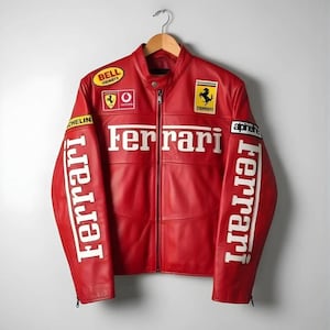 Op de afbeelding: Rode leren jas met het Ferrari-logo en witte belettering. De jas heeft een ritssluiting, diverse patches en het woord "Ferrari" op de mouwen. De jas hangt aan een houten hanger.