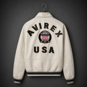 May include: Cream-colored leather jacket with the word "AVIREX" across the back, along with "USA" and a circular patch featuring the American flag. The jacket has black and white striped cuffs and hem.