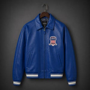 May include: A bright blue leather jacket with a collared neckline and a zip-up front. The jacket has a chest patch with "AVIREX" and an American flag design. White and blue striped detailing is on the cuffs and hem. The jacket is hung on a wooden hanger.