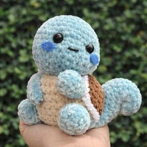 May include: A handmade, light blue crochet turtle plushie with a tan belly and a brown shell. The turtle has black eyes and blue cheek accents. The plushie is soft and cuddly, perfect for a child's toy or nursery decor.