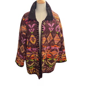 May include: A long-sleeved jacket in a dark brown base colour featuring a vibrant geometric pattern in shades of orange, pink, yellow, and lime green. The jacket has a solid dark brown collar, a front button closure, and black trim along the edges.