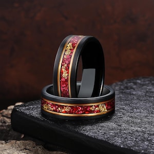 Peut inclure: Deux bagues noires avec incrustation rouge et or. Les bagues ont une finition noire polie avec une bande dorée de chaque côté de l'incrustation rouge. L'incrustation rouge a un aspect texturé avec des paillettes dorées.