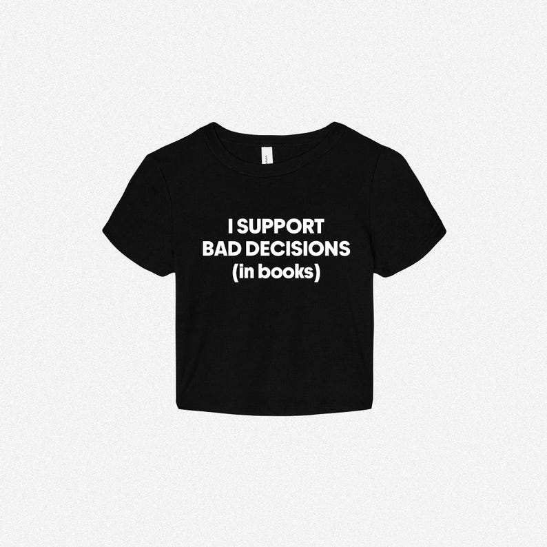 May include: A black short-sleeved crop top featuring the white text "I SUPPORT BAD DECISIONS (in books)" printed across the center of the chest. The garment has a crew neckline and a straight hemline, constructed from a solid black fabric.