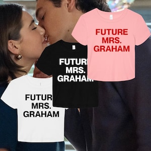 Peut inclure: Trois t-shirts à manches courtes et col rond en rose, noir et blanc. Chaque t-shirt porte l'inscription "FUTURE MRS. GRAHAM" imprimée dans une police sans empattement en gras. Le rose a du texte rouge, le noir du texte blanc et le blanc du texte noir.