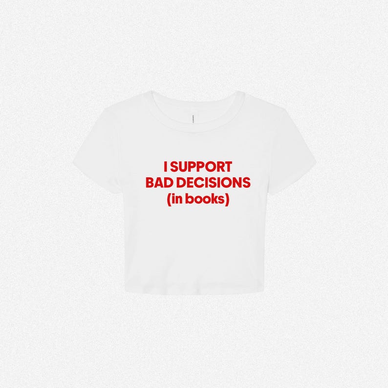 May include: A white short-sleeved crop top featuring the red text I SUPPORT BAD DECISIONS (in books) printed in a bold, sans-serif font across the center of the chest. The garment has a crew neckline and a cropped hemline.