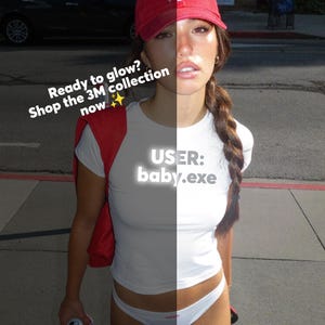 Peut inclure: Une femme porte un t-shirt blanc avec le texte "USER: baby.exe" et des sous-vêtements blancs. Elle porte une casquette de baseball rouge et un pull rouge sur les épaules. L'image comprend également le texte "Ready to glow? Shop the 3M collection now".