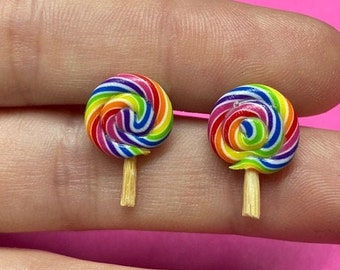 Könnte beinhalten: Ein Paar Regenbogen-Lollipop-Ohrringe mit Holzstielen. Die Ohrringe befinden sich auf einem Finger.