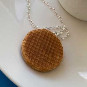 May include: A silver chain necklace with a round brown waffle cookie pendant.