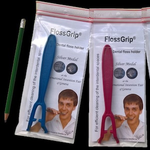 May include: Three dental floss holders in blue, red, and green, each in a clear plastic package. The packages feature the text "FlossGrip" and "Silver Medal" with an image of a person using the product. A green pencil is on the left.