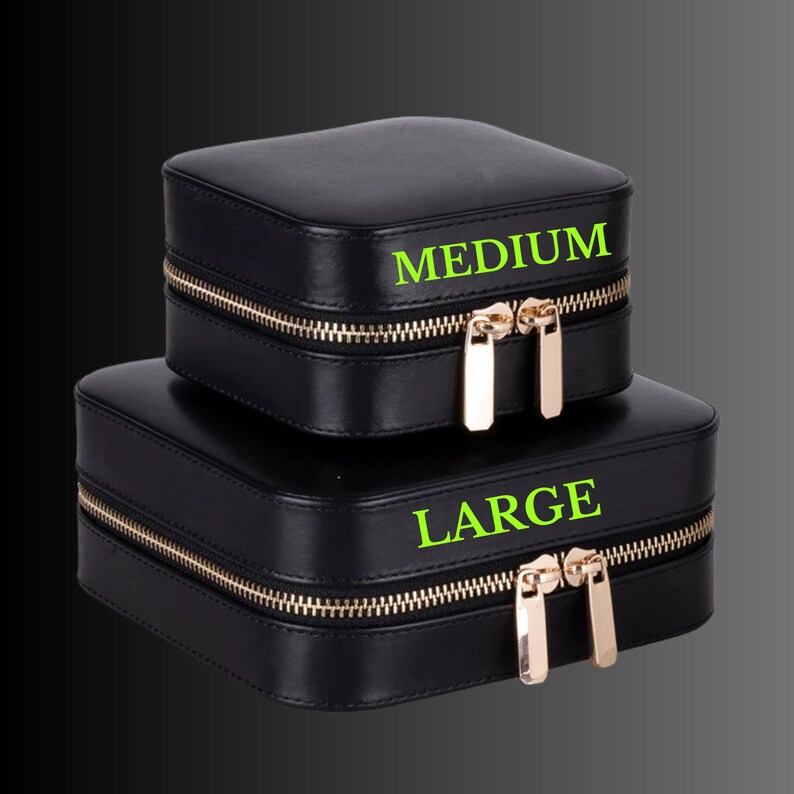 K&ouml;nnte beinhalten: Zwei schwarze quadratische Schmuckk&auml;stchen, eines mit der Aufschrift "MEDIUM" und das andere mit "LARGE". Beide Boxen haben goldfarbene Rei&szlig;verschl&uuml;sse und Ziehgriffe. Die Boxen sind vor dunklem Hintergrund gestapelt.
