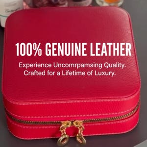 K&ouml;nnte beinhalten: Eine rote, quadratische Schmuckkassette aus Leder mit goldenem Rei&szlig;verschluss und Ziehern. Der Text "100% GENUINE LEATHER" ist auf der Vorderseite abgebildet. Zus&auml;tzlicher Text lautet "Experience Uncomrpamsing Quality. Crafted for a Lifetime of Luxury."