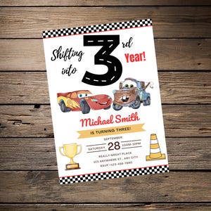 May include: A birthday invitation with cartoon car illustrations, a trophy, and a traffic cone. The text reads "Shifting into 3rd Year!" and includes party details. The invitation is on a wooden background.