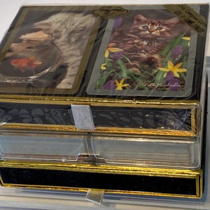 May include: A set of two decks of playing cards featuring a cat and a goldfish. The cards are packaged in a black box with gold trim and a clear plastic cover. The box has the text "Collector's Edition" and "Be at the Ready" printed on it.