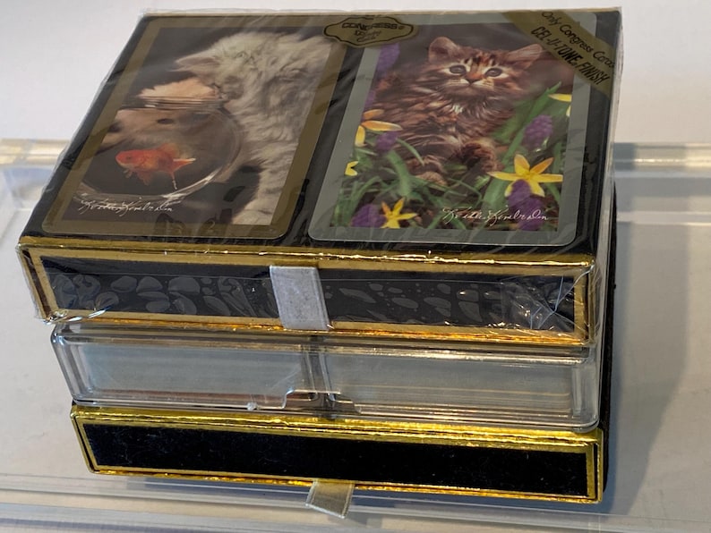 May include: A set of two decks of playing cards featuring a cat and a goldfish. The cards are packaged in a black box with gold trim and a clear plastic cover. The box has the text "Collector's Edition" and "Be at the Ready" printed on it.