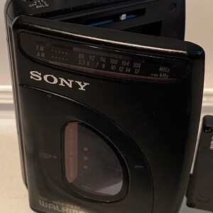 May include: Black Sony Walkman FM/AM radio with a silver headphone jack. The radio has a tuning dial, volume control, and frequency display. The model number is WM-FX21.