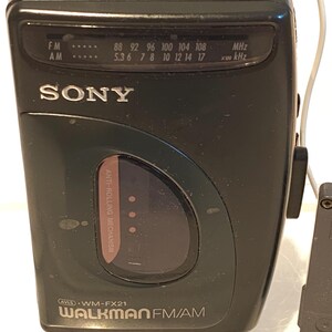 May include: Black Sony Walkman FM/AM radio with a tuning dial and frequency display. The radio has a headphone jack and the text "WALKMAN FM/AM" is visible. The radio is a vintage electronic device.