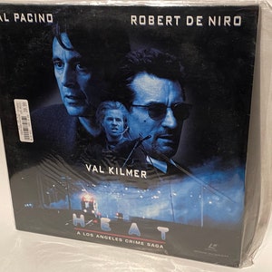 May include: A DVD case featuring a blue and black image of Al Pacino, Robert De Niro, and Val Kilmer from the movie "Heat". The text "A Los Angeles Crime Saga" is printed on the bottom of the case.