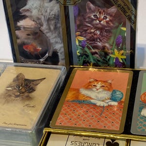 May include: A deck of Congress playing cards with a Cel-U-Tone finish. The box features images of kittens and a goldfish. The cards are in a black box with gold trim. The ace of spades is visible in the bottom right corner.