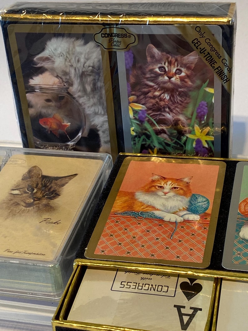 May include: A deck of Congress playing cards with a Cel-U-Tone finish. The box features images of kittens and a goldfish. The cards are in a black box with gold trim. The ace of spades is visible in the bottom right corner.