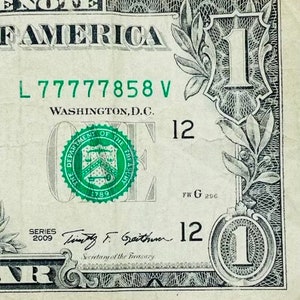 May include: A one dollar bill with a green seal featuring the Department of the Treasury and the year 1789. The bill has the serial number L77777858 V and the signature of Timothy F. Geithner, Secretary of the Treasury. The bill is dated 2009.
