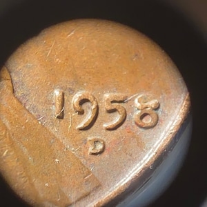 May include: Close-up of a copper-colored penny with the year 1958 stamped on the back.