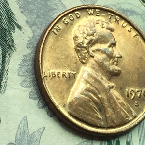 May include: A copper-colored 1970 US penny with the words "In God We Trust" and "Liberty" inscribed on it. The profile of Abraham Lincoln is visible on the coin.
