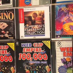 May include: A collection of CD-ROM software boxes. Titles include "Hoyle Casino", "Compton's Reference Collection", "King's Quest", and "Web Clip Empire". The boxes are in clear plastic cases, with various graphics and text.