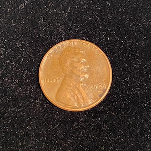 May include: A copper-colored 1949 Lincoln penny. The coin features the profile of Abraham Lincoln, with the inscriptions "IN GOD WE TRUST" and "LIBERTY". The year "1949" is also visible.