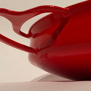 May include: A red enameled cast iron casserole dish with two large handles. The dish is oval shaped and has a glossy finish.